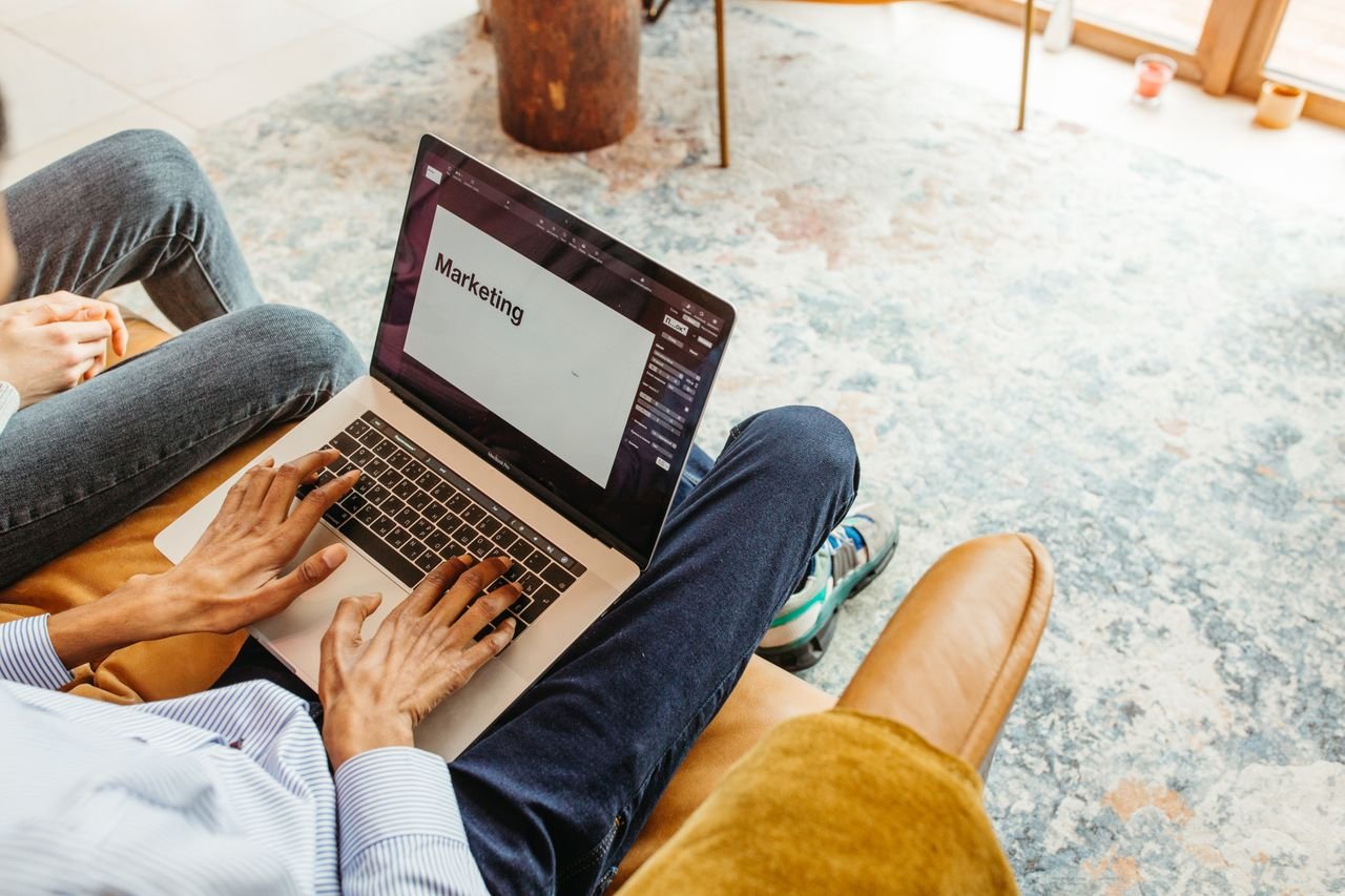 Menu Young adult typing on a laptop for marketing work, seated indoors in a casual setting.